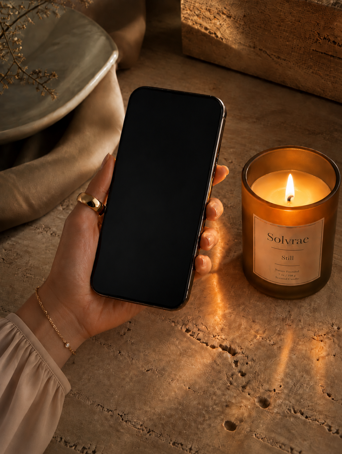 A hand holding a phone beside a glowing amber candle
